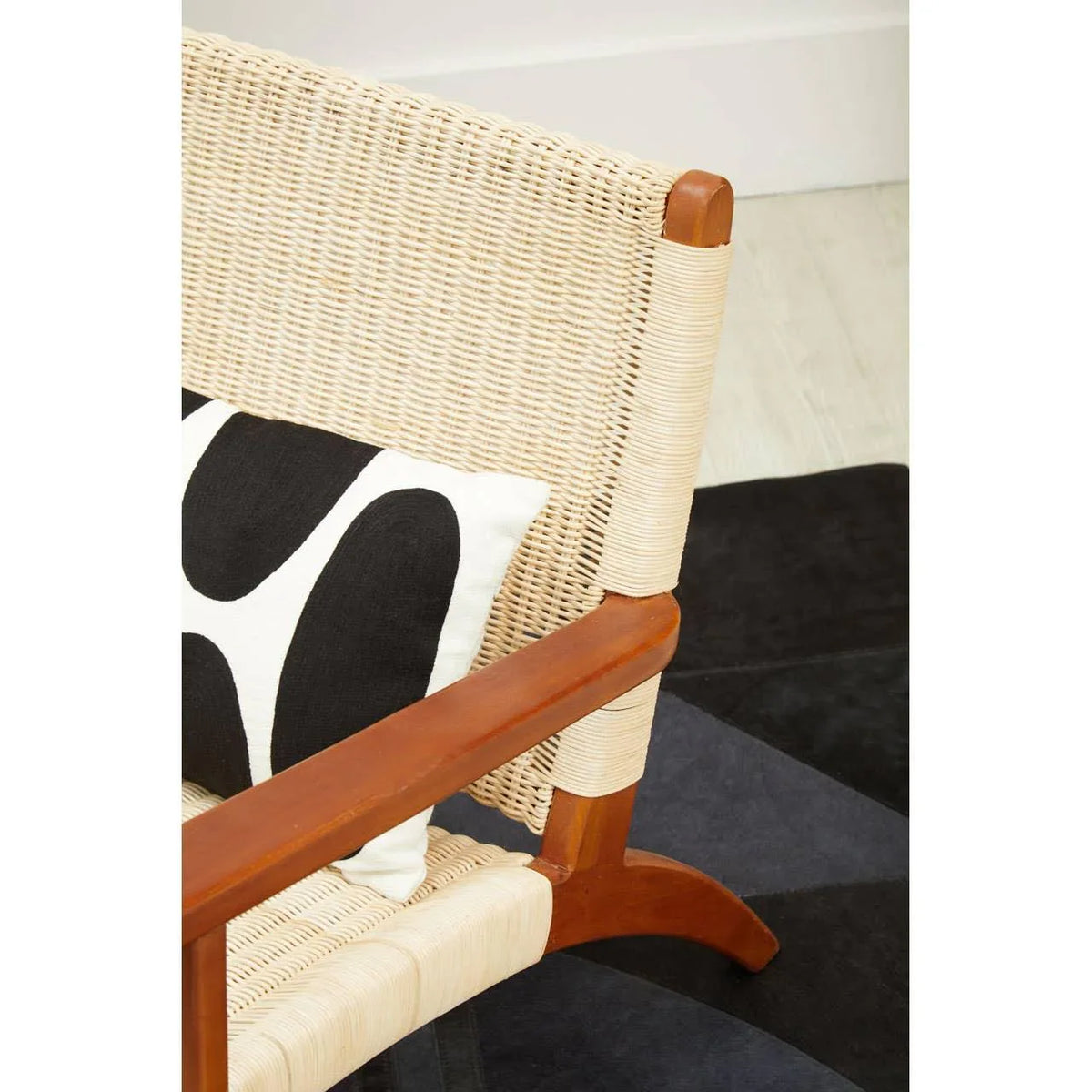 Woven rattan armchair with wooden frame and modern black and white cushion on rug