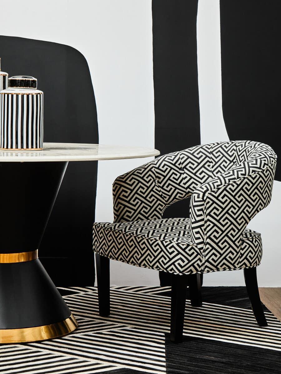 Black and white patterned accent chair with curved back next to round marble dining table