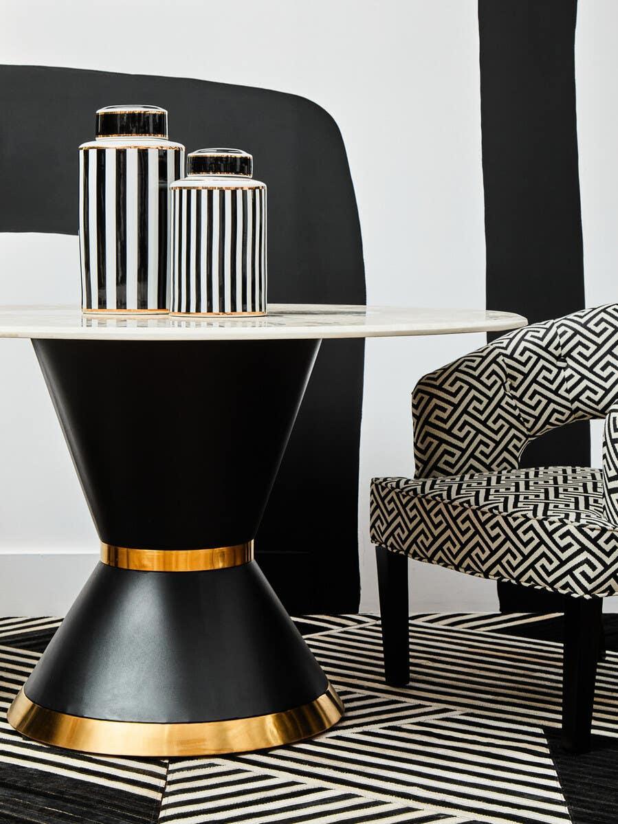 Modern dining table with black and gold base, marble top, striped vases, patterned armchair