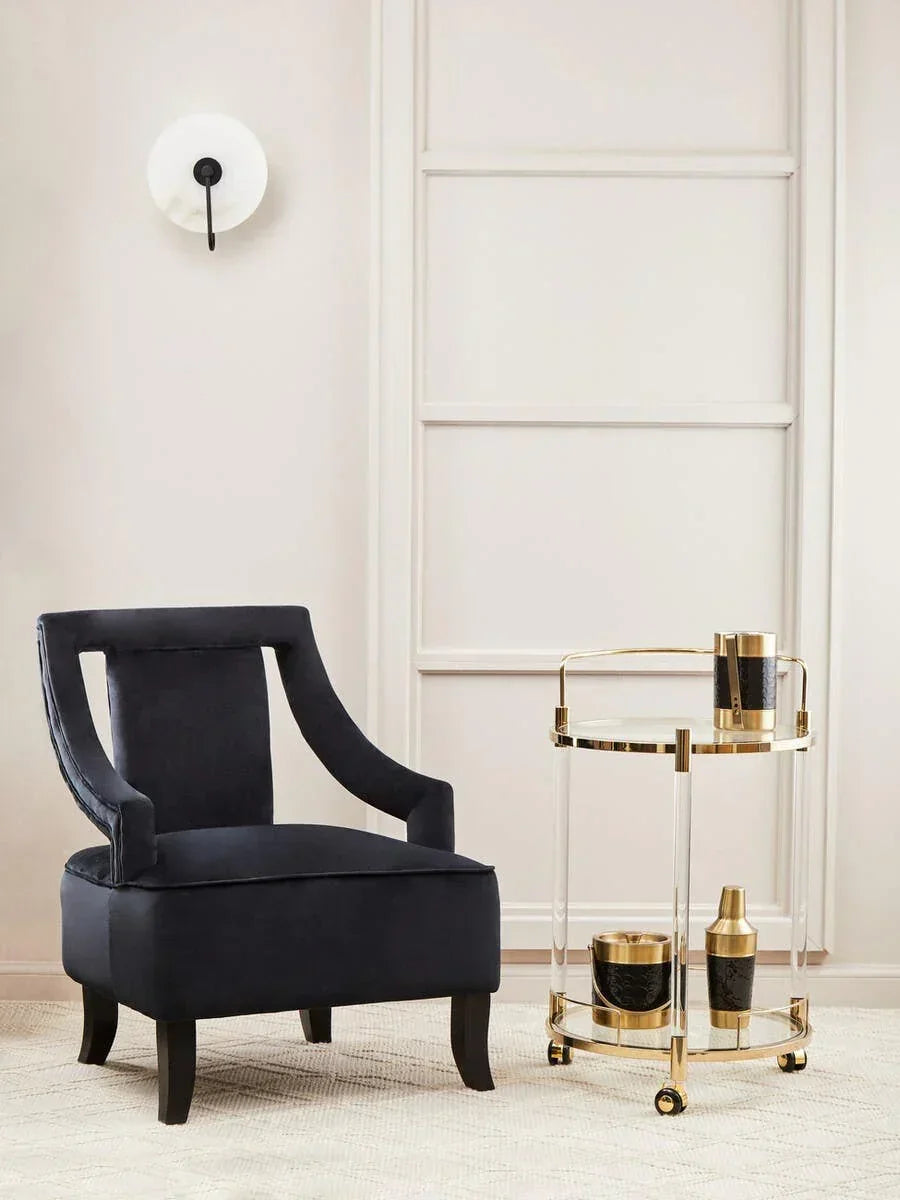 Velvet accent chair with open arms beside gold and glass drinks trolley on beige rug