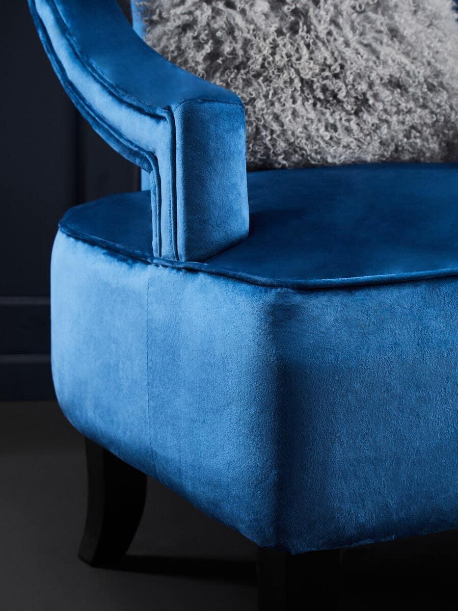 Close-up of blue velvet armchair with curved armrest and black wooden legs