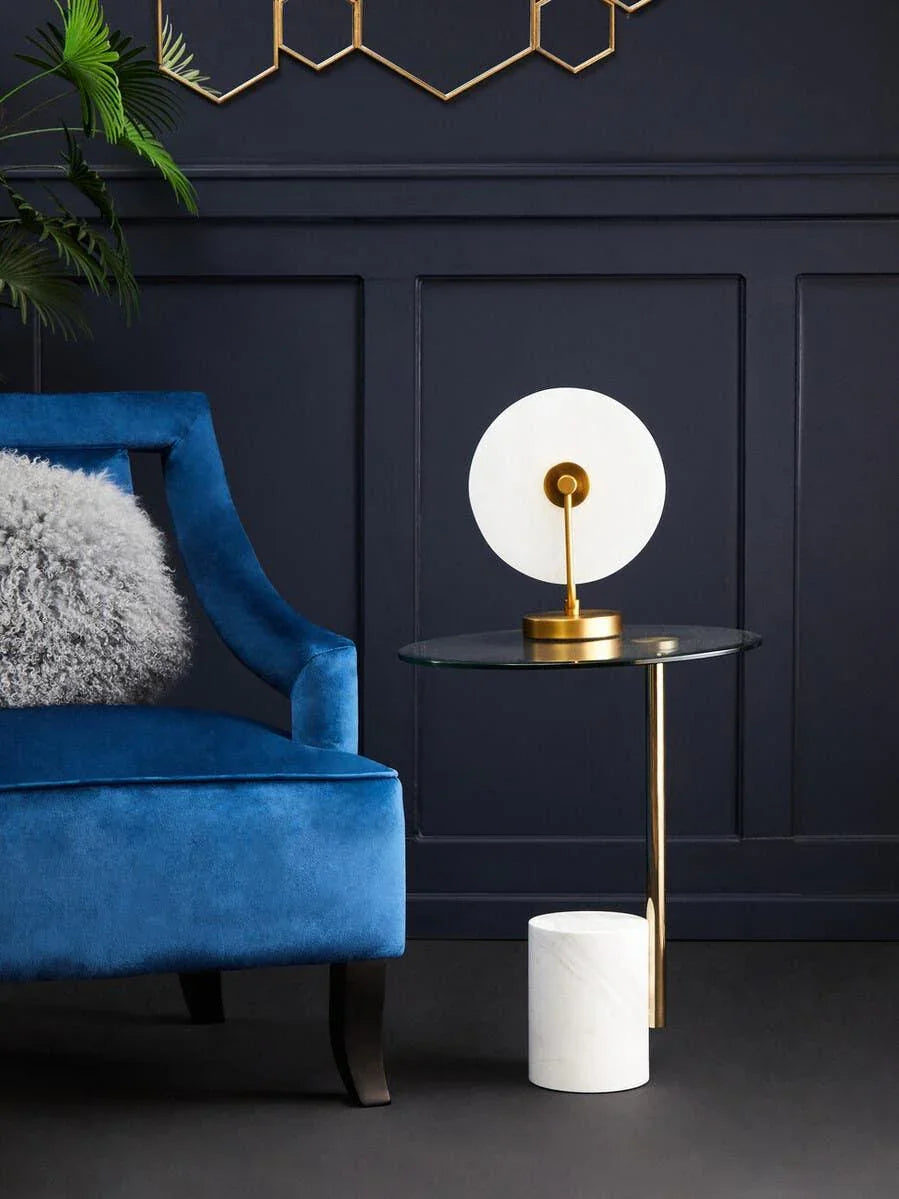 Blue velvet armchair beside glass and gold side table with marble base