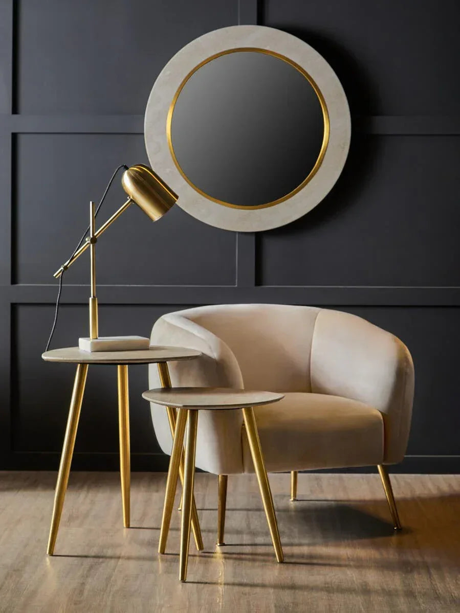 Velvet armchair with gold legs, nesting side tables, and round wall mirror in modern living room