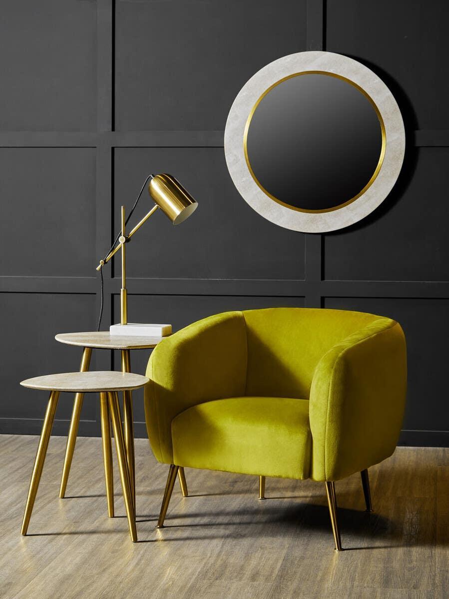 Mustard yellow velvet accent chair with gold legs beside marble nesting tables and round wall mirror