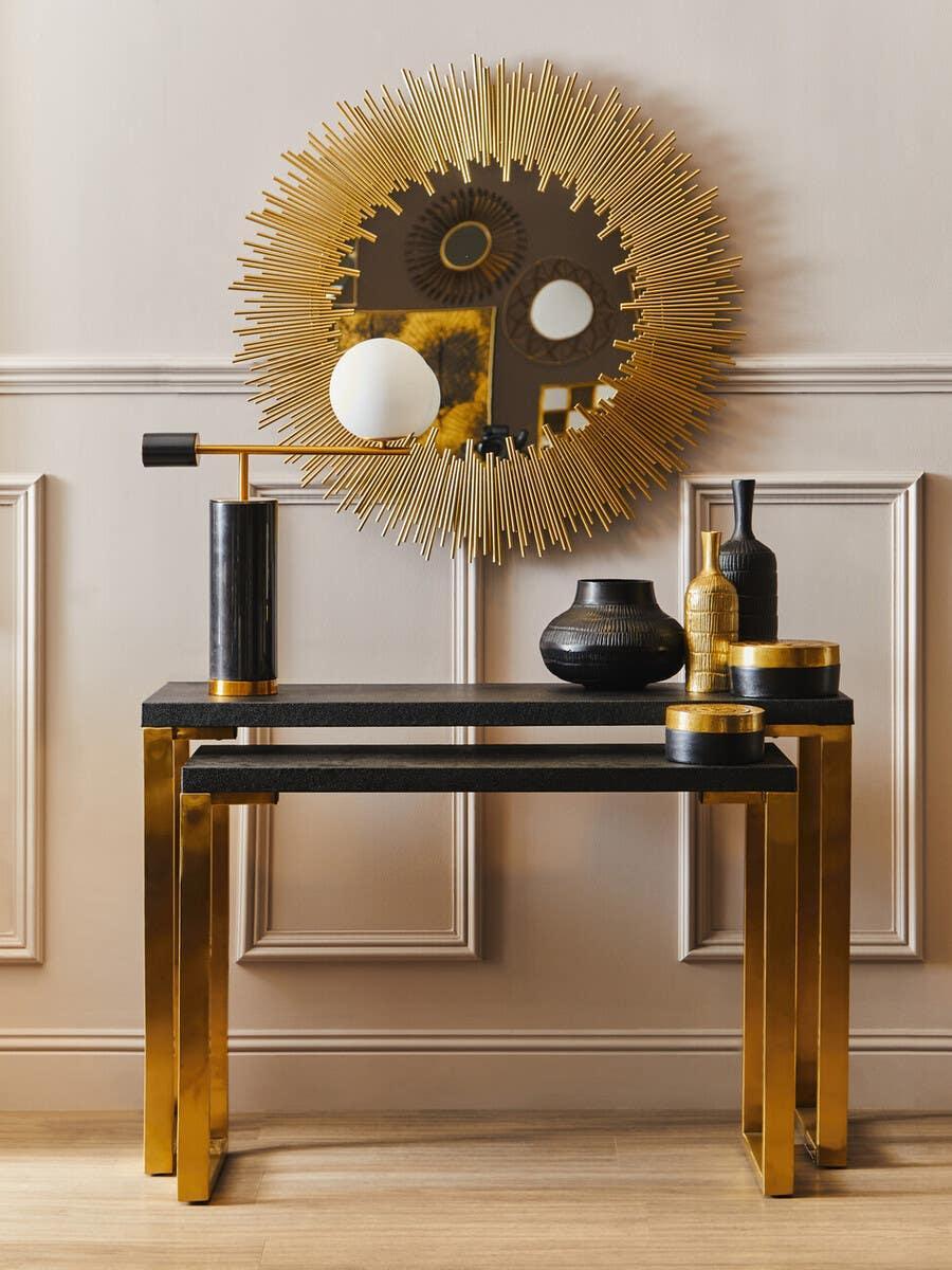 Black and gold console table with decorative vases and a round sunburst wall mirror