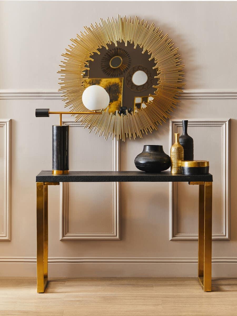 Gold console table with black top, sunburst wall mirror, and decorative vases in hallway