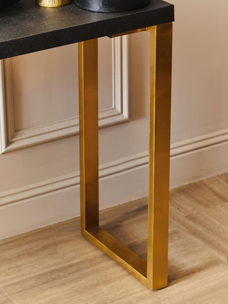 Gold metal table leg with black textured tabletop on wood floor