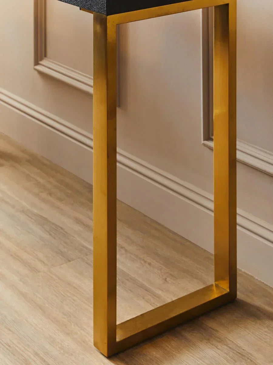 Gold metal table leg with black tabletop on wood floor beside panelled wall