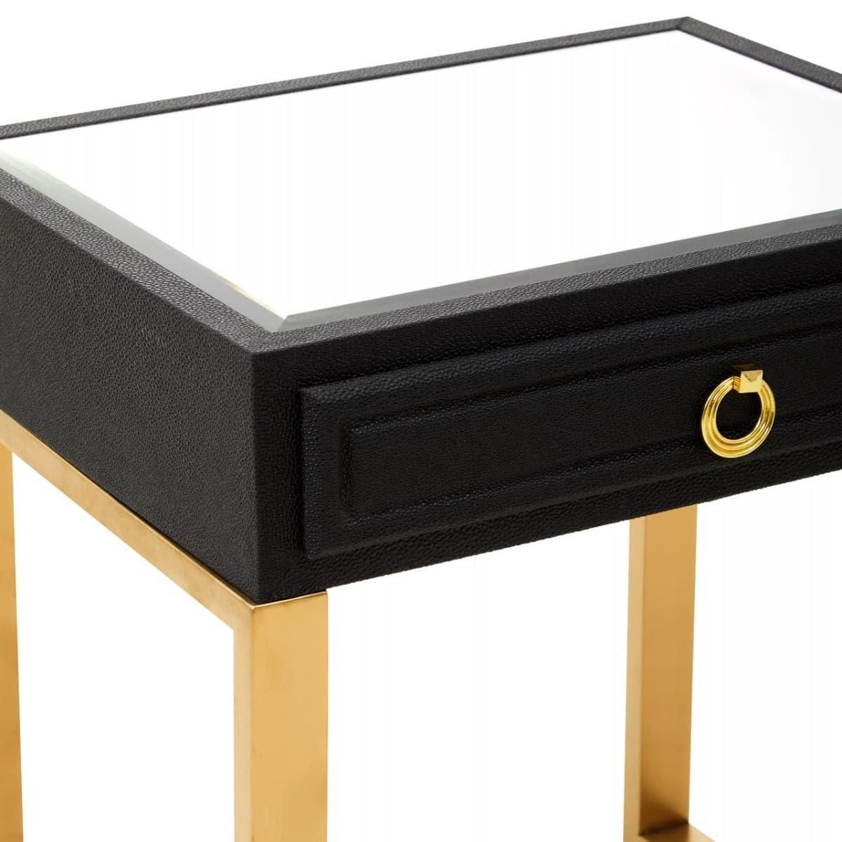 Black bedside table with gold legs and drawer pull, glass top surface