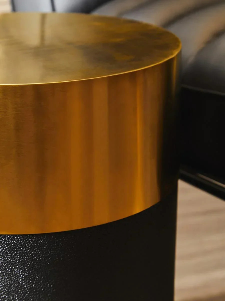 Round gold metal side table with textured black base next to black leather sofa