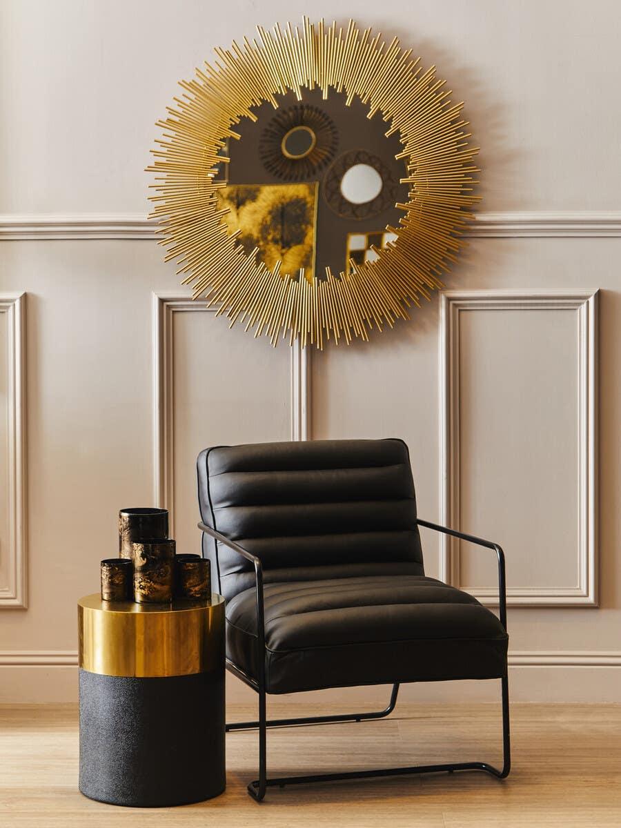 Black leather accent chair with gold side table and sunburst wall mirror in modern living room