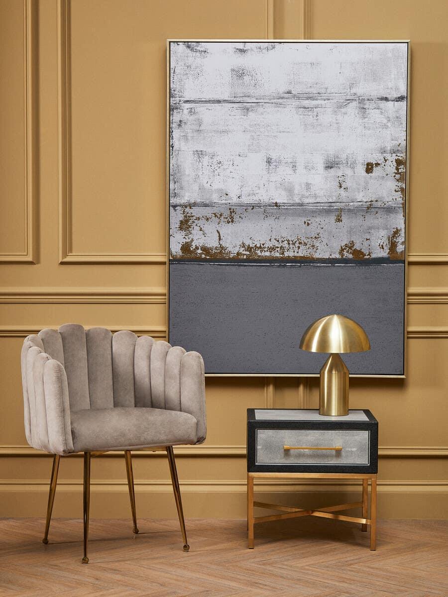 Grey velvet accent chair with gold legs, metallic table lamp, and modern bedside table