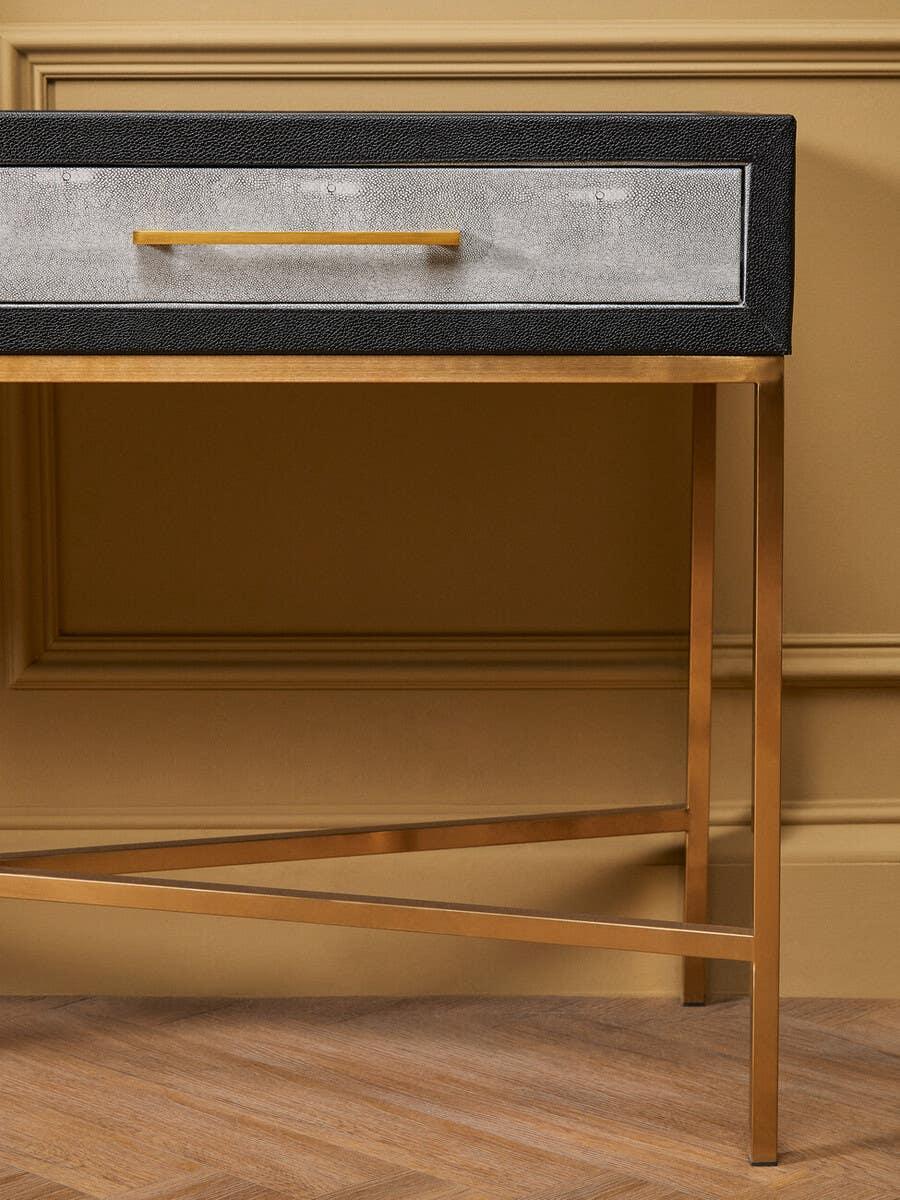 Modern console table with gold metal legs and textured drawer front against paneled wall