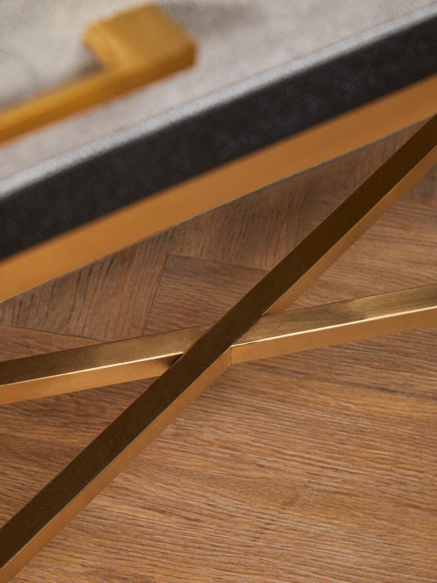Gold metal legs detail of a modern coffee table with light wood herringbone flooring