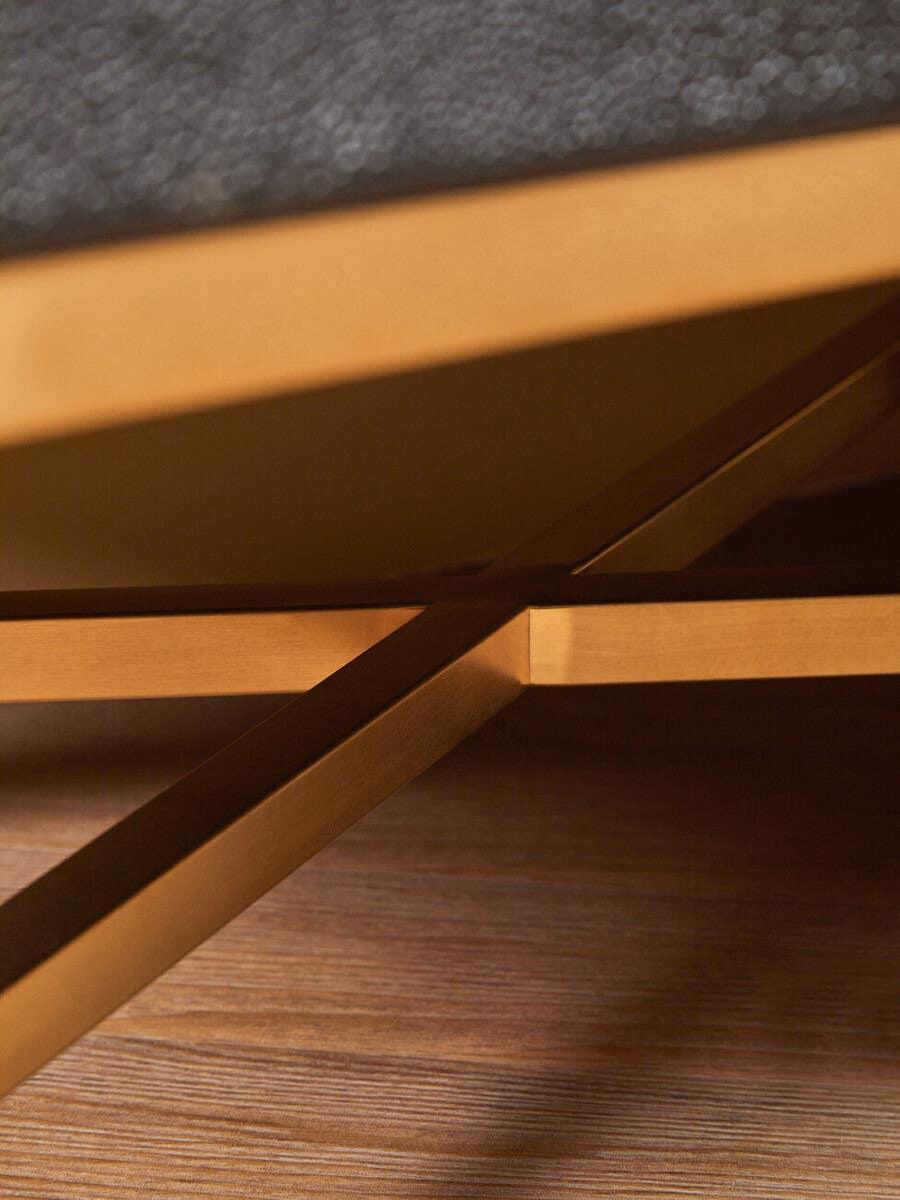 Close view of gold metal table legs and wooden floor beneath a textured dark tabletop