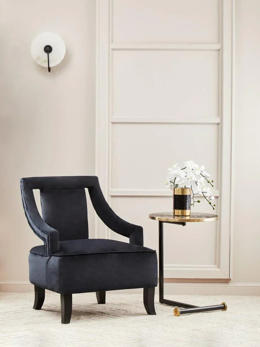 Black velvet accent chair beside round marble side table with gold trim in modern living room