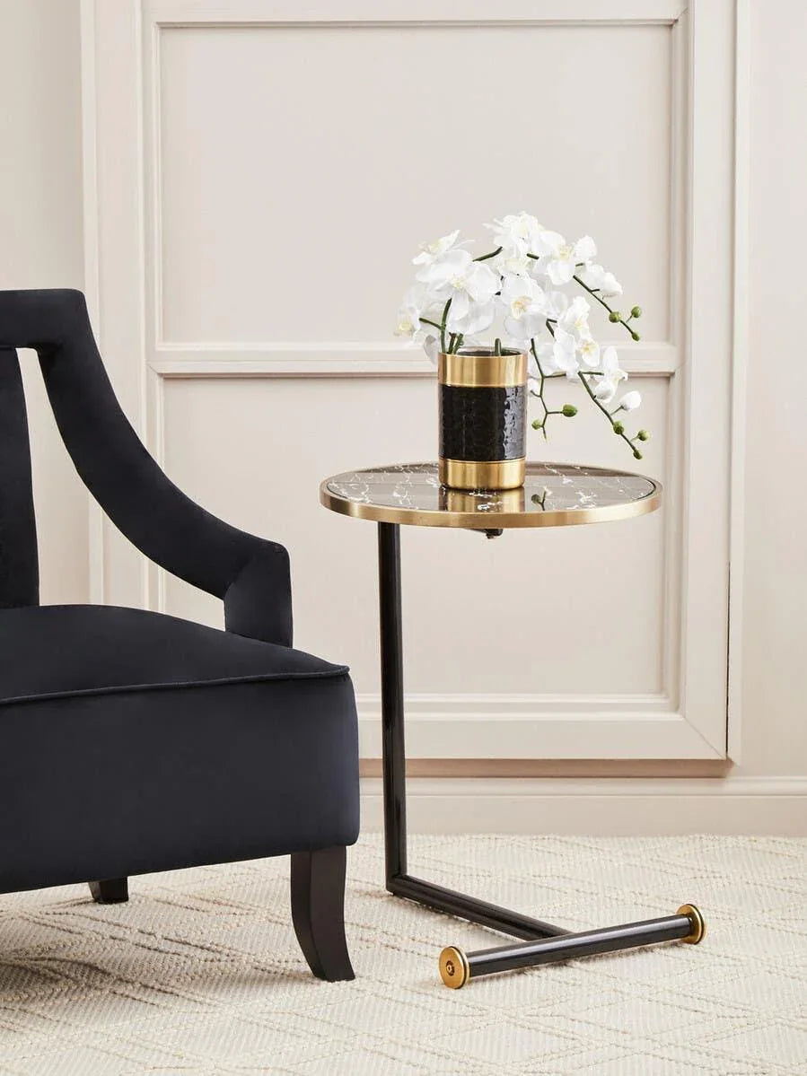 Black marble top side table with gold trim beside a dark velvet armchair on beige carpet