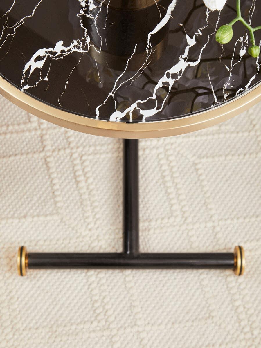 Black marble top side table with gold trim and black metal base on textured rug