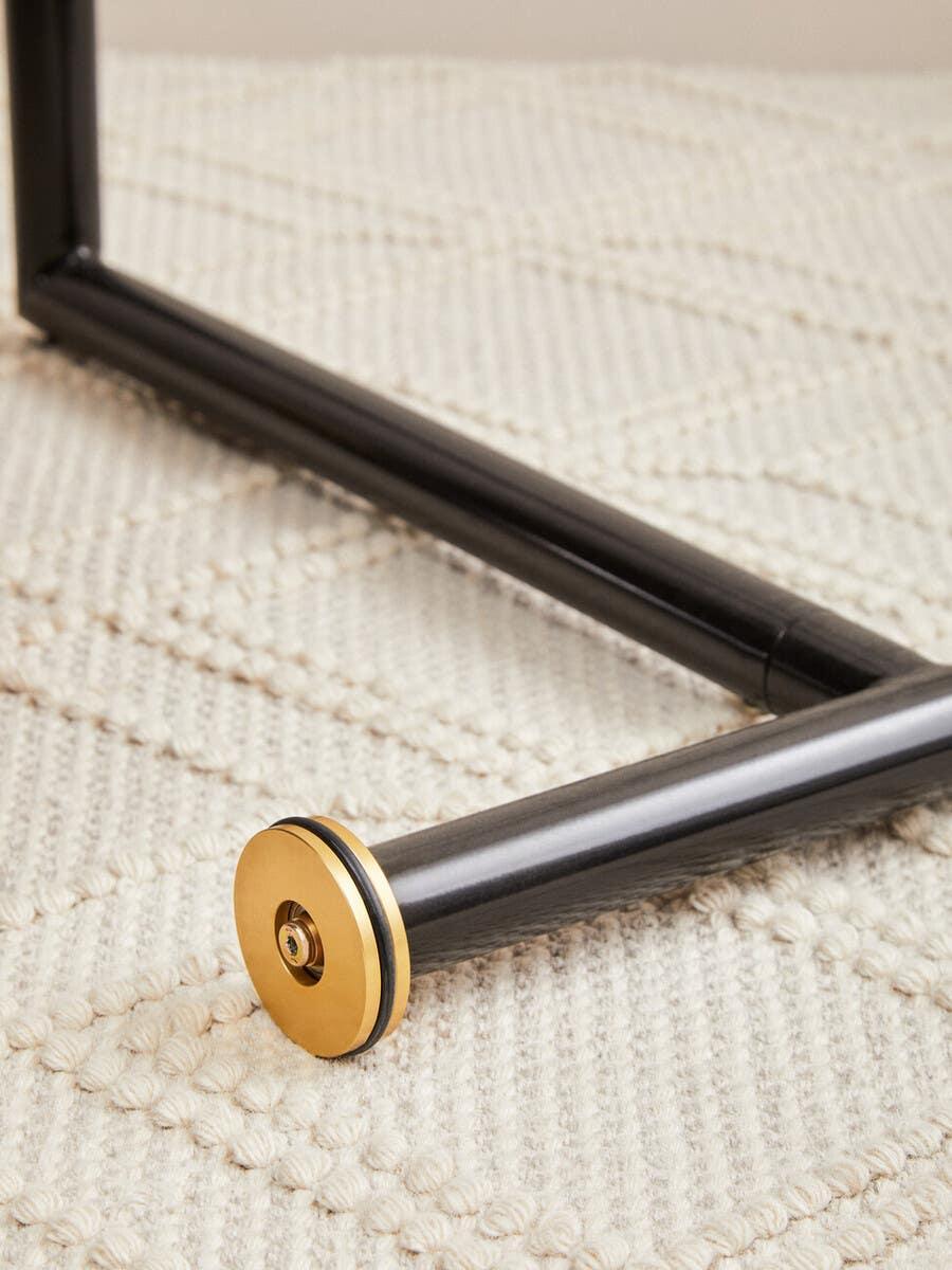 Black metal furniture leg with gold accent detail on textured cream rug