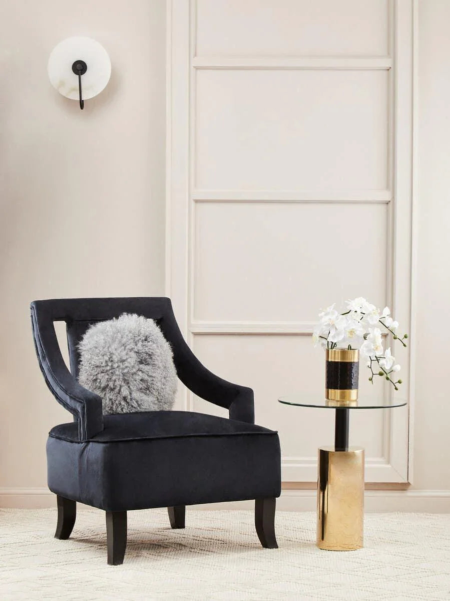 Black velvet accent chair with grey cushion beside gold and glass side table with white flowers