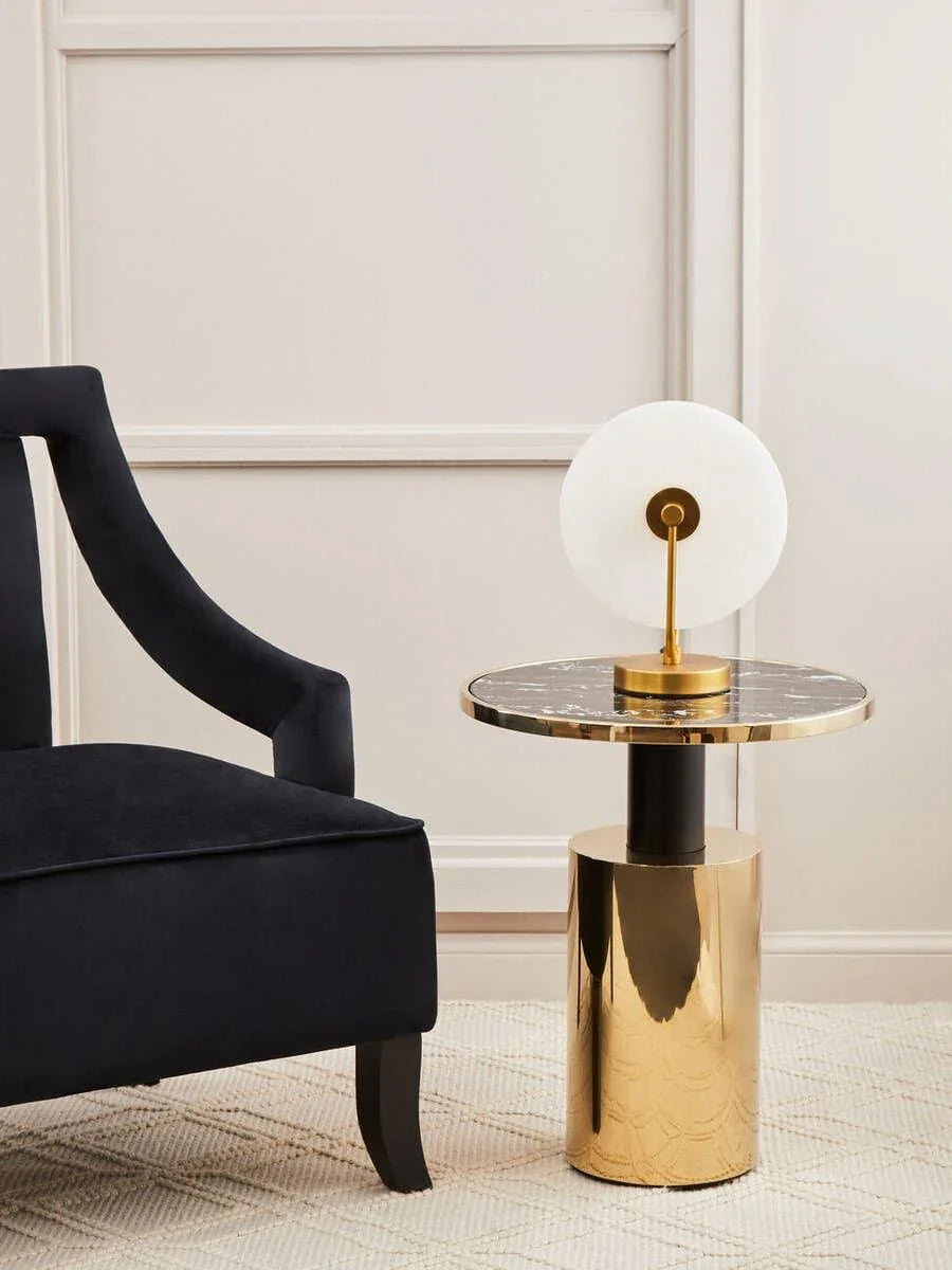 Black velvet armchair beside round marble and gold side table with modern table lamp