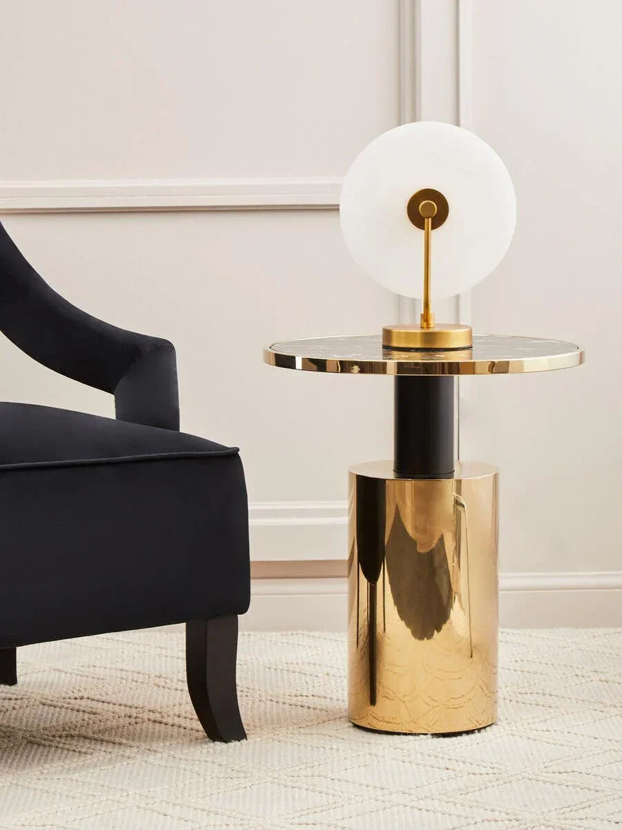 Contemporary gold side table with black marble top beside dark armchair in living room