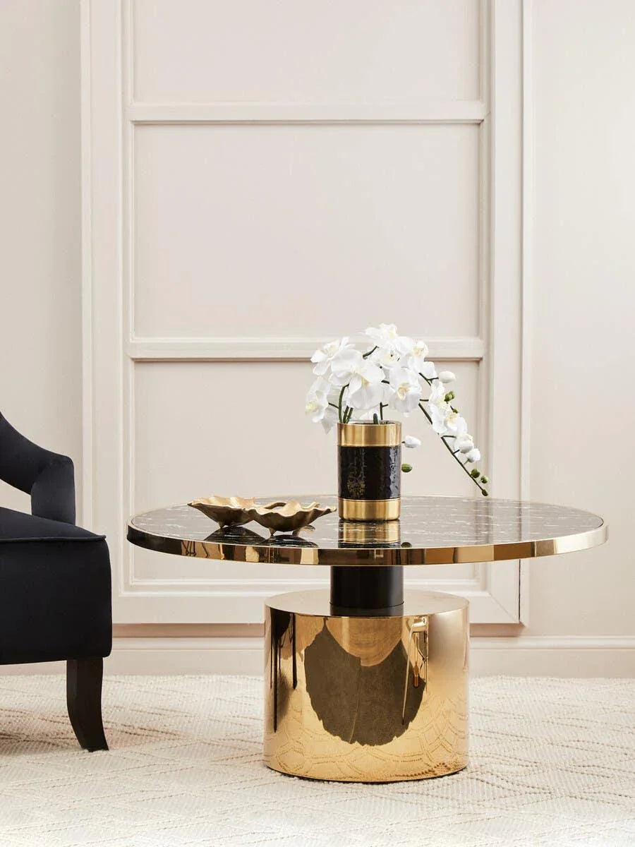 Round black and gold coffee table with gold decorative bowl and orchid arrangement