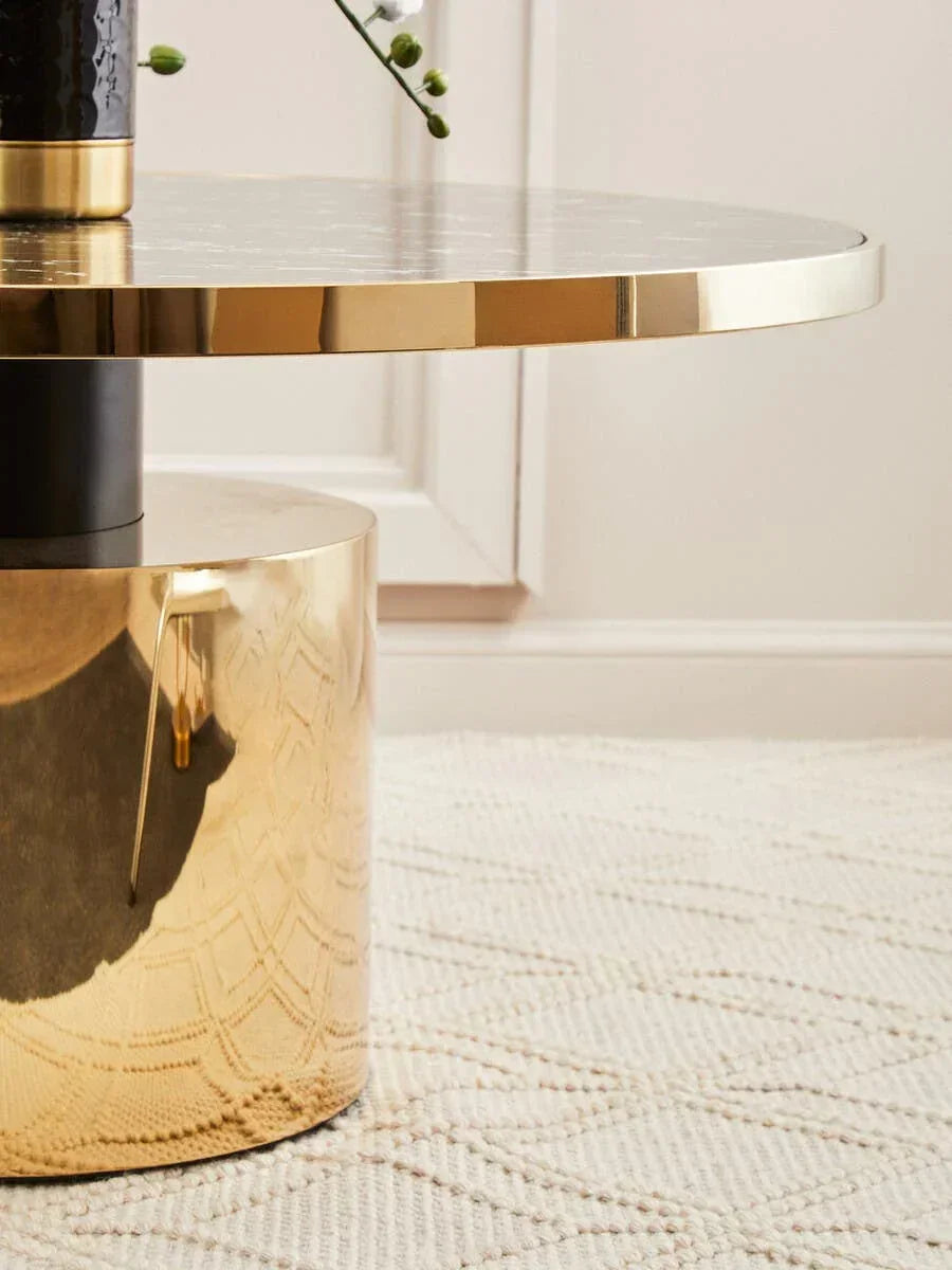 Gold coffee table with round marble top and reflective base on textured cream rug