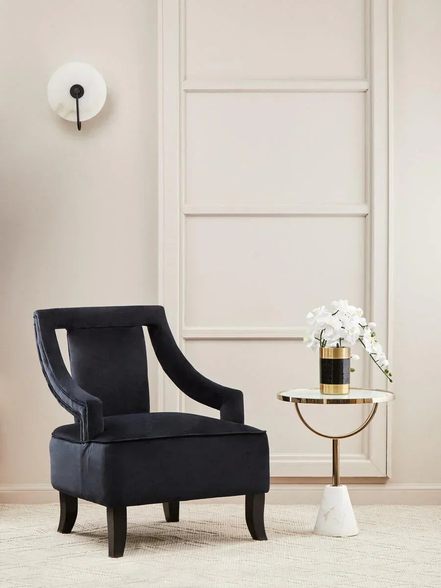 Black velvet accent chair with curved arms beside round marble side table and flower arrangement