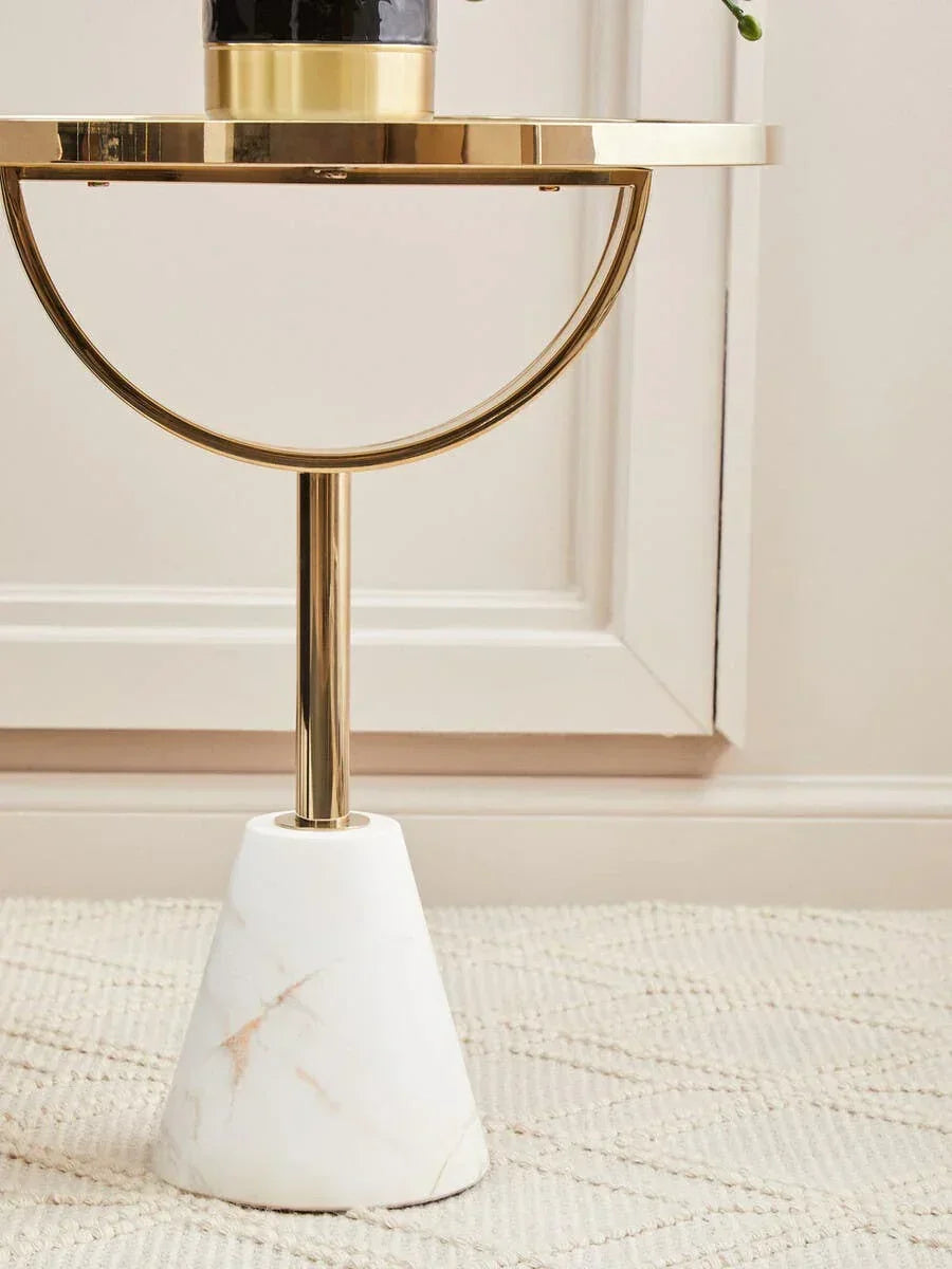 Gold side table with marble base and round top on patterned beige rug