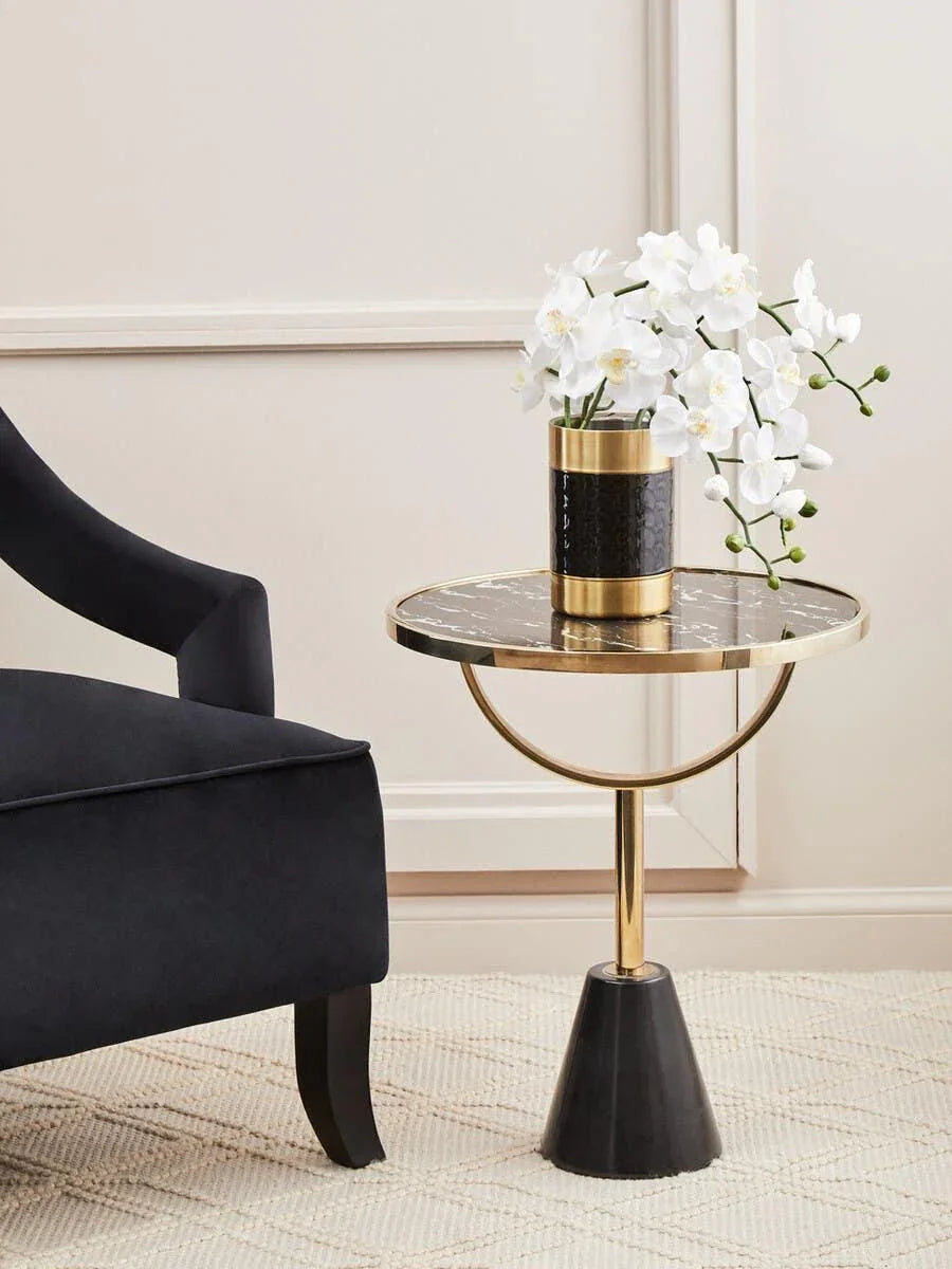 Black and gold side table with marble top beside black armchair, white orchid in vase