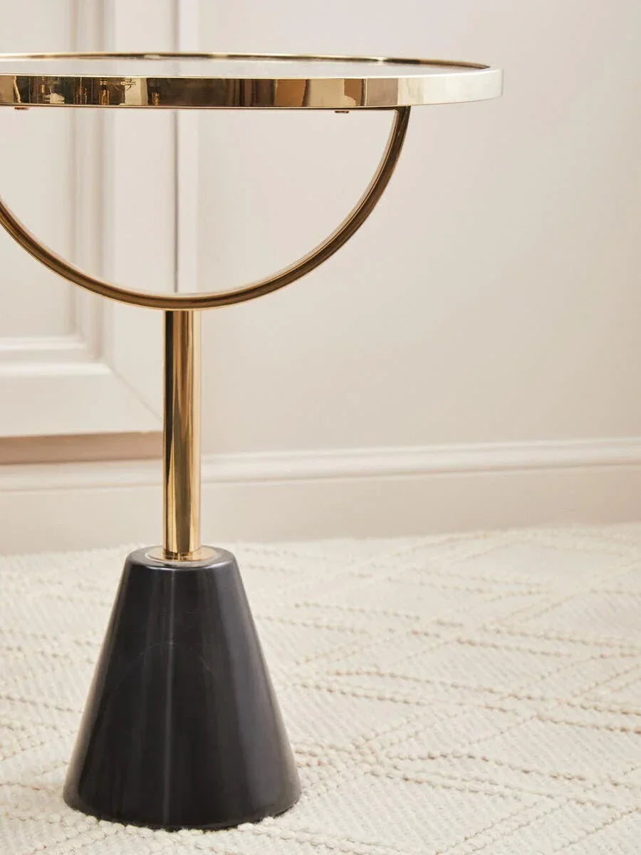 Gold metal side table with black marble base on textured cream rug