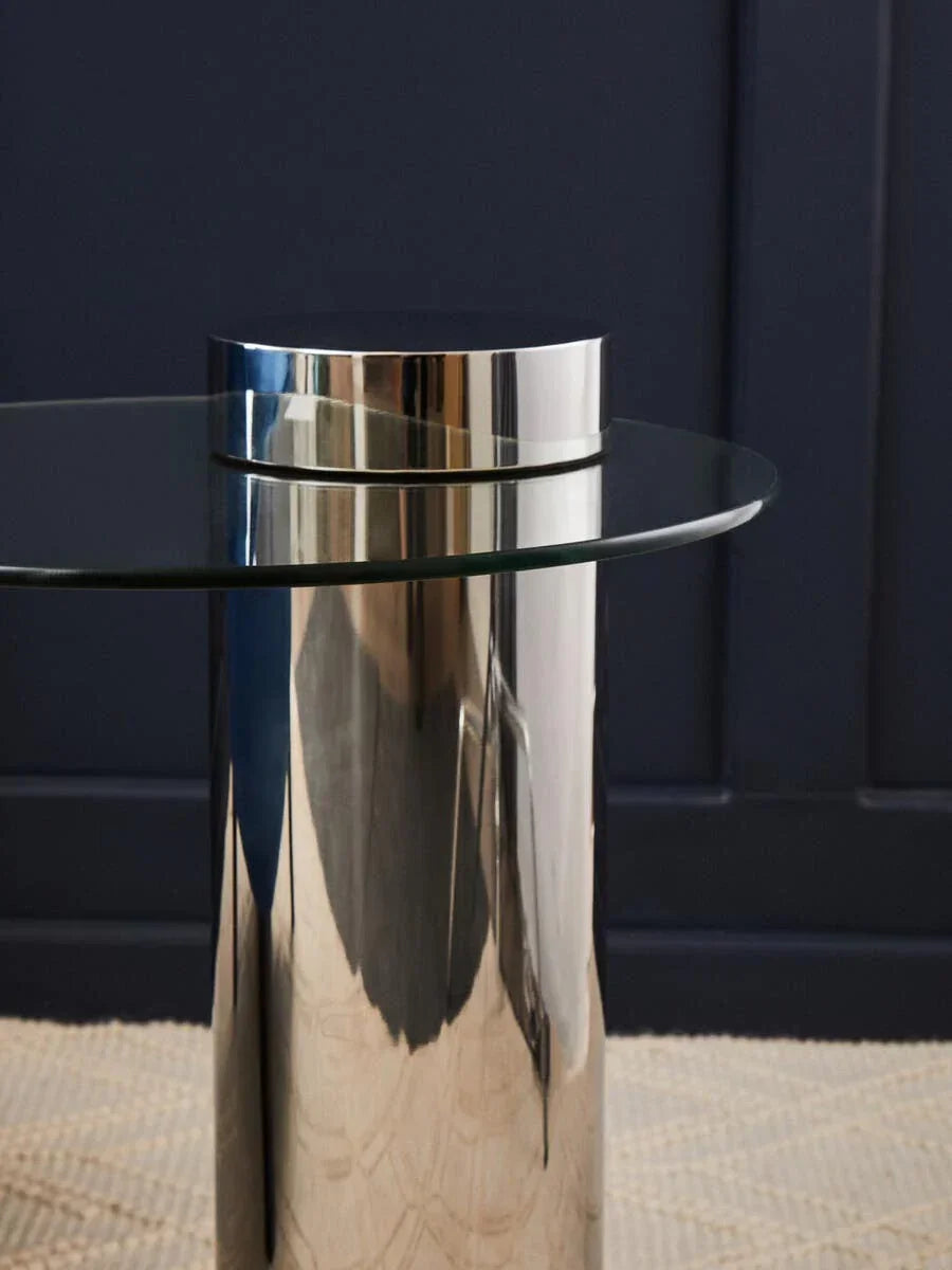 Round glass top side table with chrome metal cylinder base on textured rug