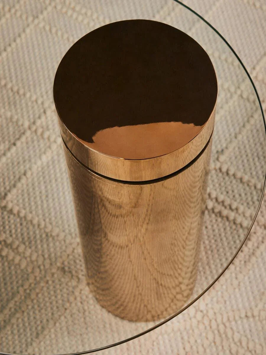 Round glass coffee table with gold metal base on textured beige rug