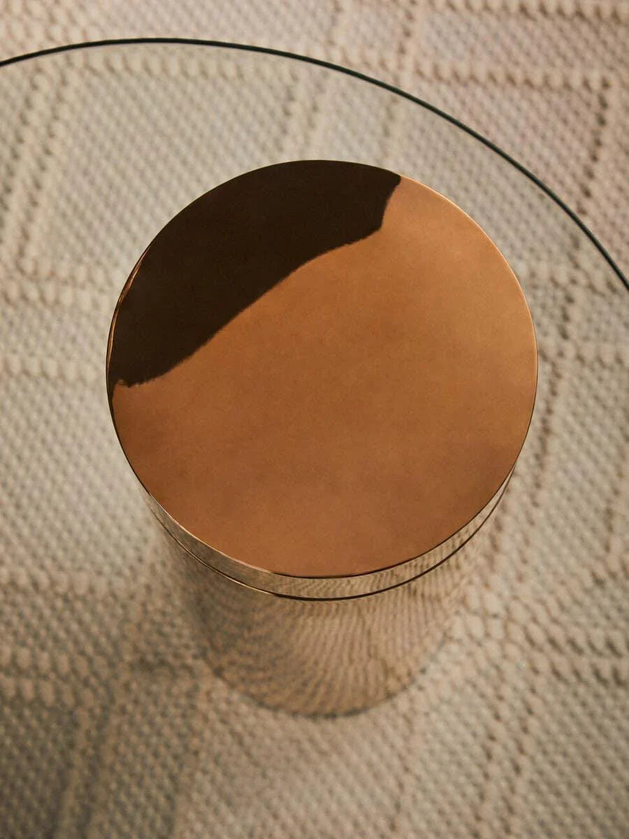 Round glass coffee table with metallic gold base on textured beige rug