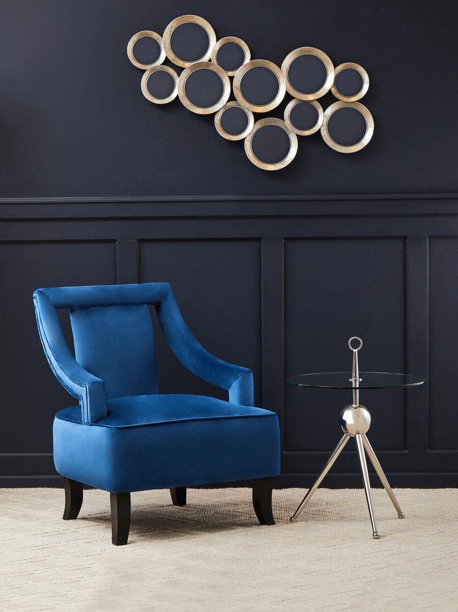 Blue velvet accent chair beside glass side table in modern living room with gold wall decor