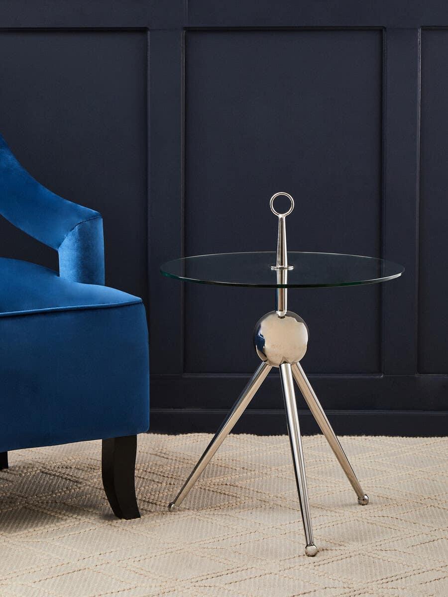 Glass top side table with chrome tripod legs beside blue velvet accent chair