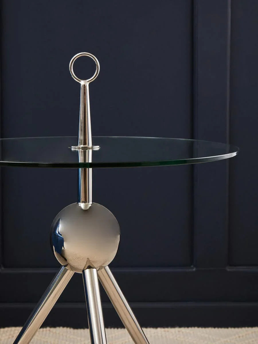 Modern glass side table with chrome tripod base and ring handle in minimalist room
