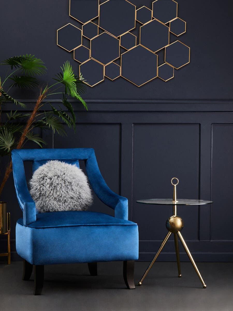 Blue velvet accent chair with grey cushion beside glass and gold side table in modern living room