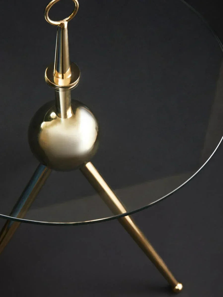 Round glass table with gold tripod legs and decorative finial detail
