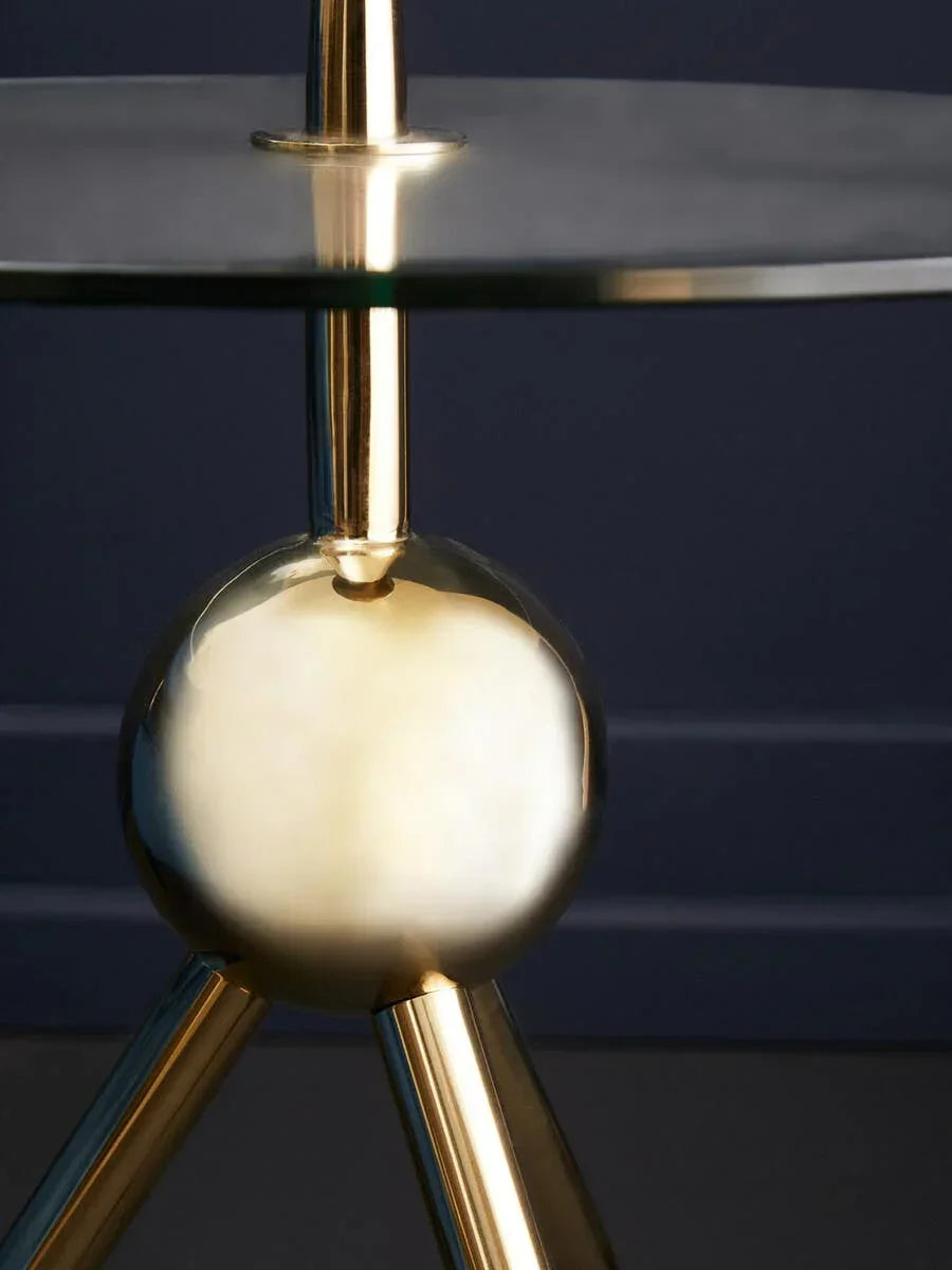 Glass side table with gold metal base and spherical accent, close-up detail