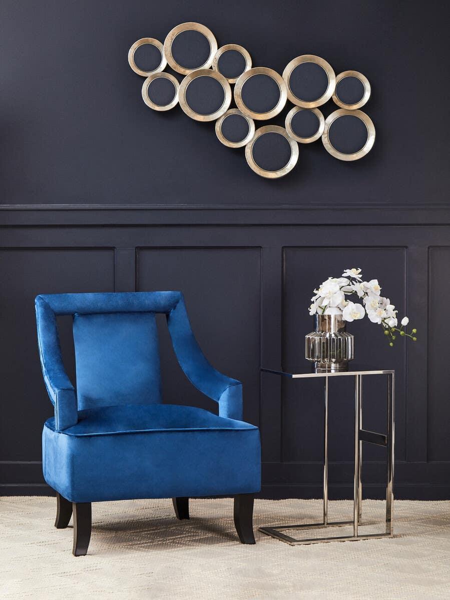 Blue velvet accent chair beside glass side table with flowers, wall art in background