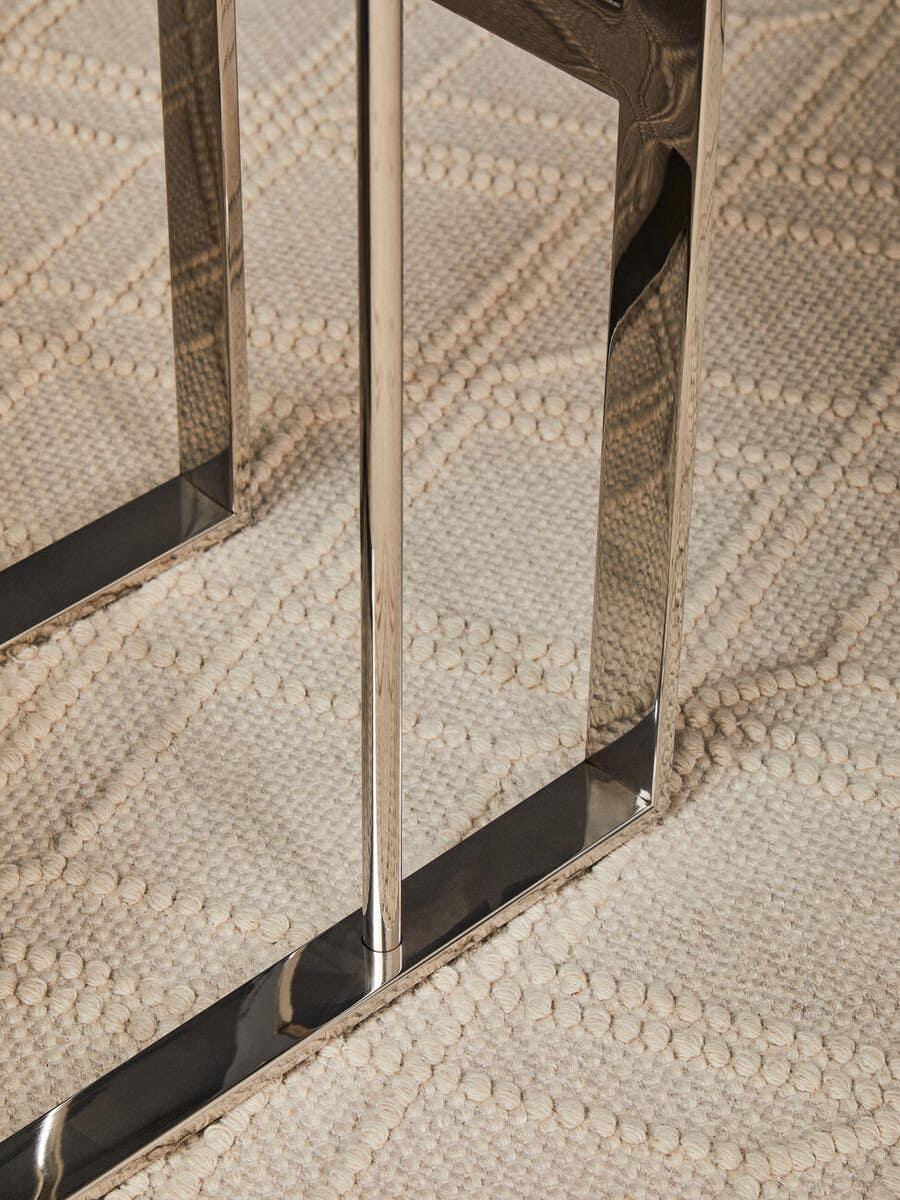 Chrome table legs on textured cream rug with geometric pattern