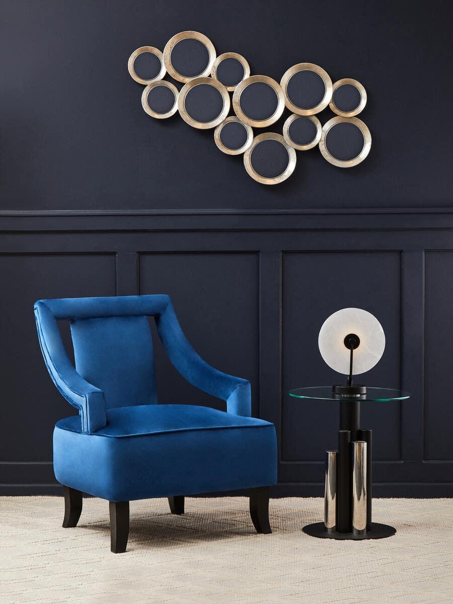 Blue velvet armchair beside glass side table and decorative wall art in modern living room