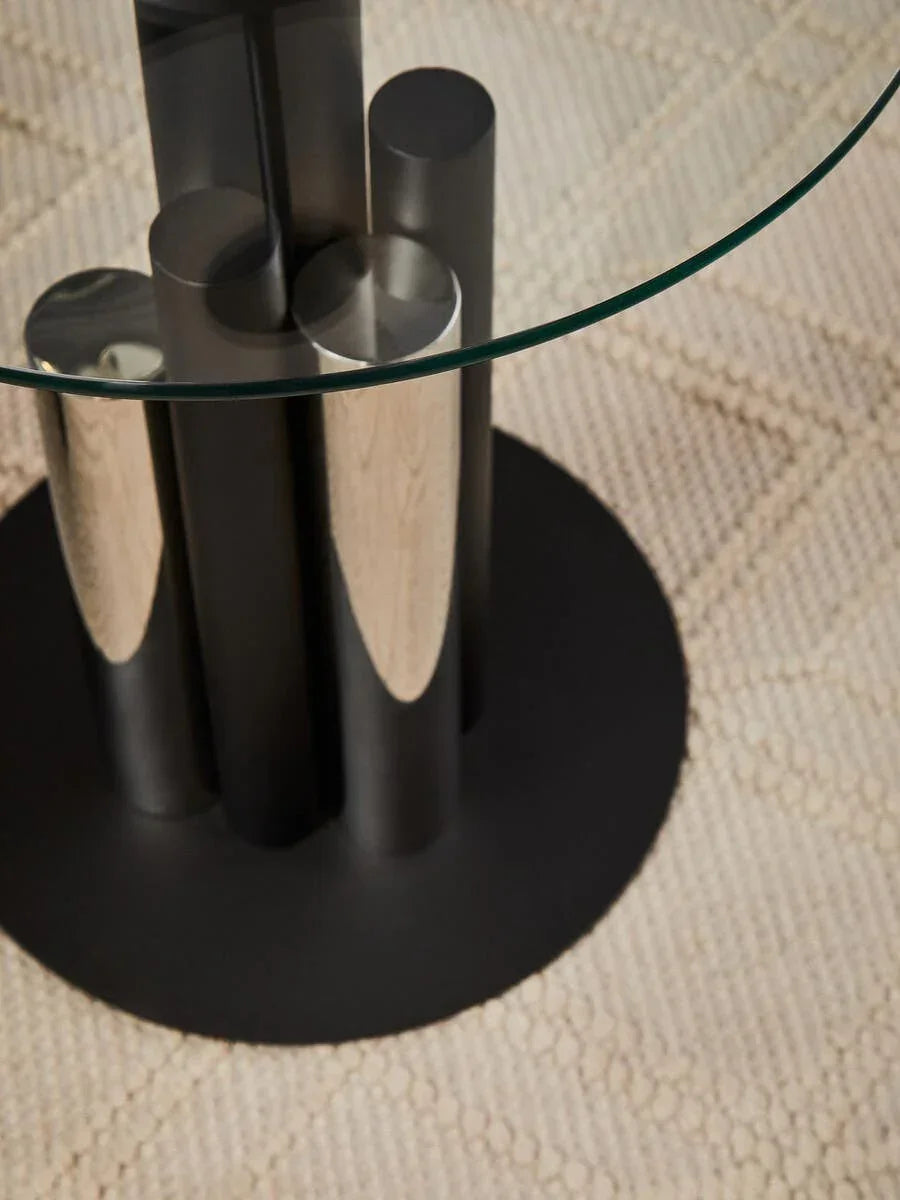Round glass dining table with black metal cylindrical base on textured cream rug