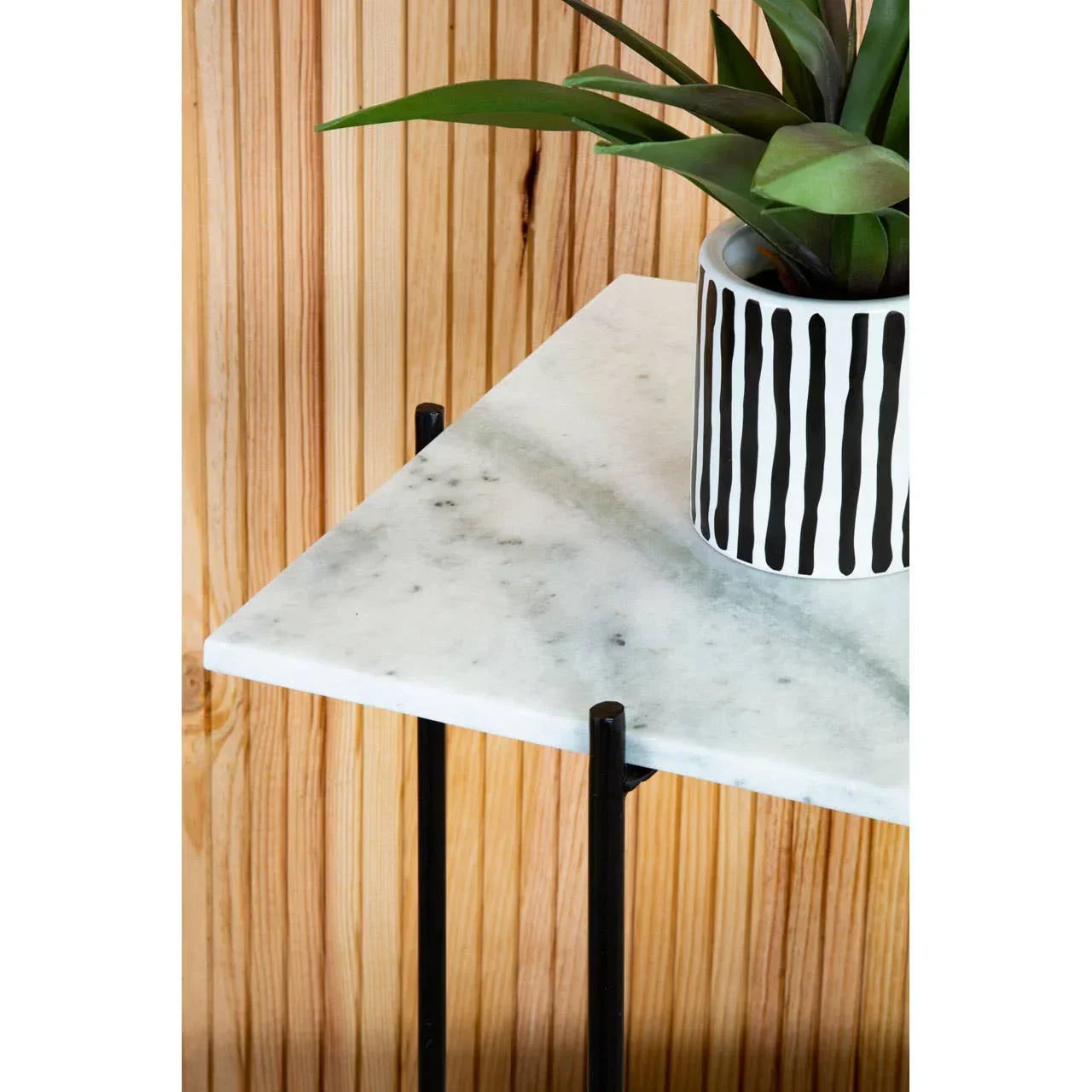 White marble side table with black metal legs and striped planter with green plant