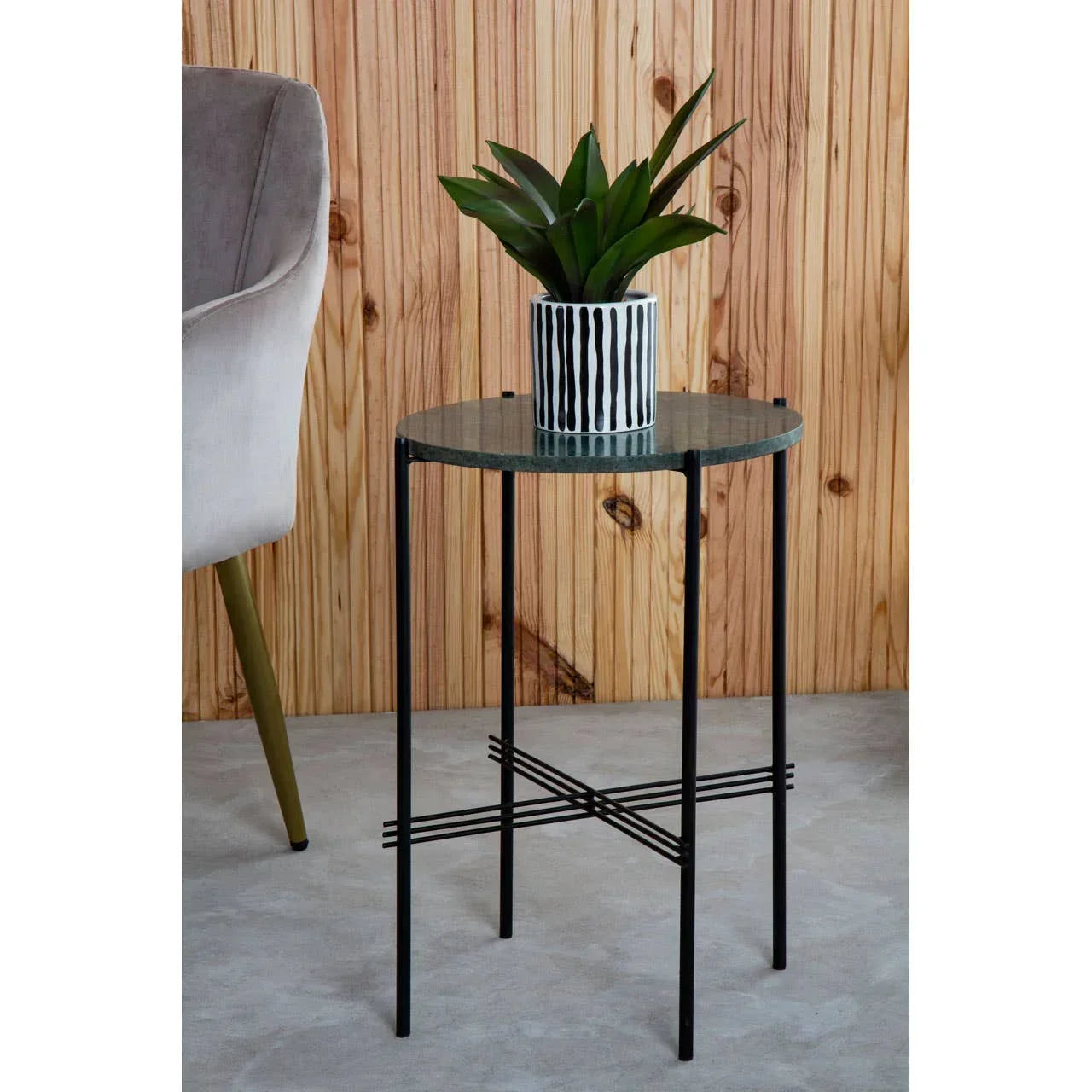 Round glass side table with black metal legs and a plant in a striped pot