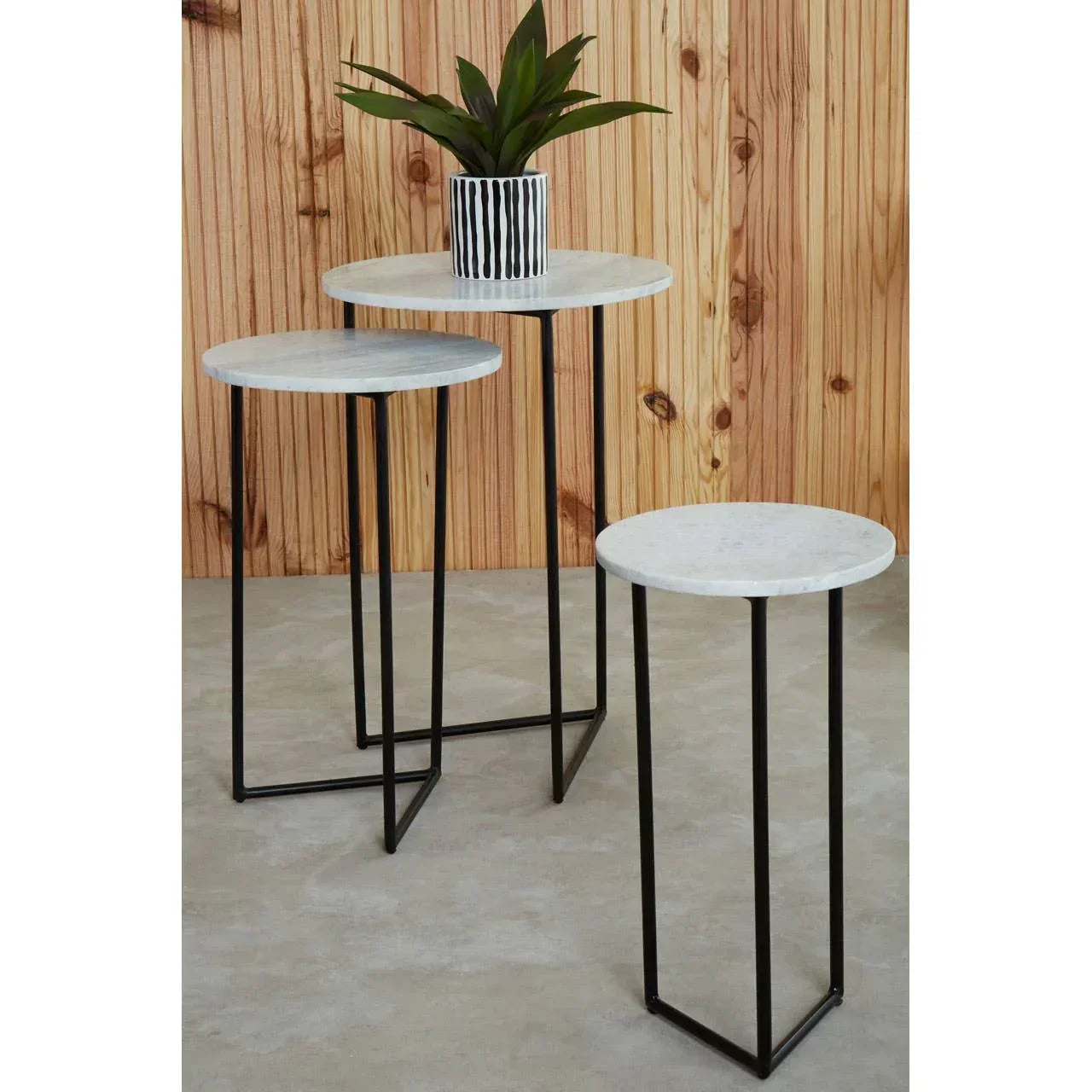 Set of three round marble side tables with black metal legs on concrete floor