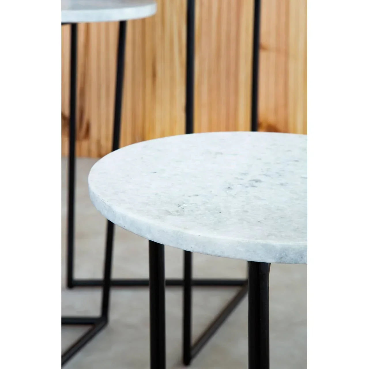 Round white marble side table with black metal legs, close-up view on wood backdrop
