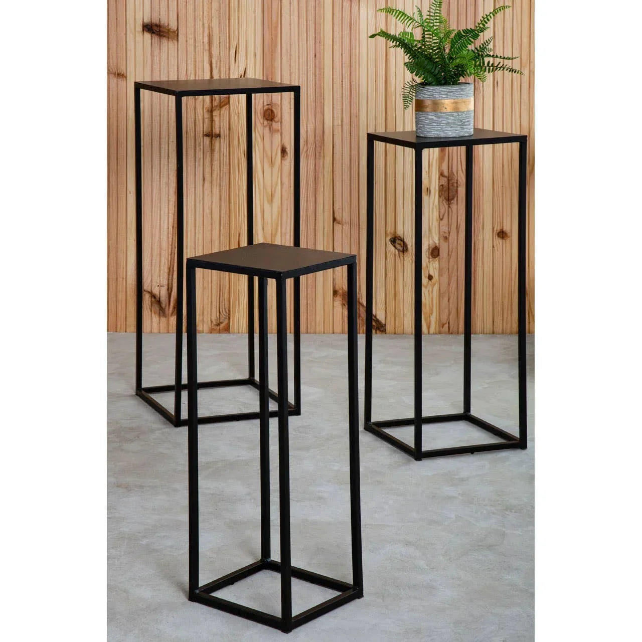 Set of three black metal plant stands with minimalist square frames on grey floor